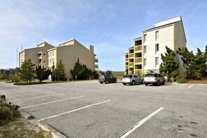 A parking lot with multiple cars, a building with balconies, and some trees. - The Oceans Unit 301 -- Oceanfront Condo with Direct Access to Pool and Beach (Nags Head)