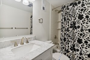 A bathroom with a white sink, a mirror, a shower curtain with a black floral pattern, and a toilet. - The Oceans Unit 301 -- Oceanfront Condo with Direct Access to Pool and Beach (Nags Head)
