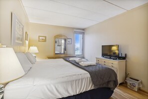 A hotel room with a bed, a TV, a desk, and a window. - The Oceans Unit 301 -- Oceanfront Condo with Direct Access to Pool and Beach (Nags Head)