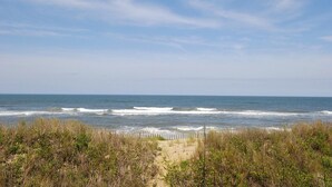 Una playa con olas, un sendero arenoso y vegetación densa.