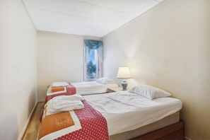 A hotel room with two beds, a window with curtains, a bedside lamp, and a view of trees outside. - The Oceans Unit 301 -- Oceanfront Condo with Direct Access to Pool and Beach (Nags Head)