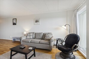 A living room with a sofa, a coffee table, a chair, and a lamp. - The Oceans Unit 301 -- Oceanfront Condo with Direct Access to Pool and Beach (Nags Head)