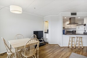 A modern kitchen with a central island, a dining area with a table and chairs, and a television. - The Oceans Unit 301 -- Oceanfront Condo with Direct Access to Pool and Beach (Nags Head)