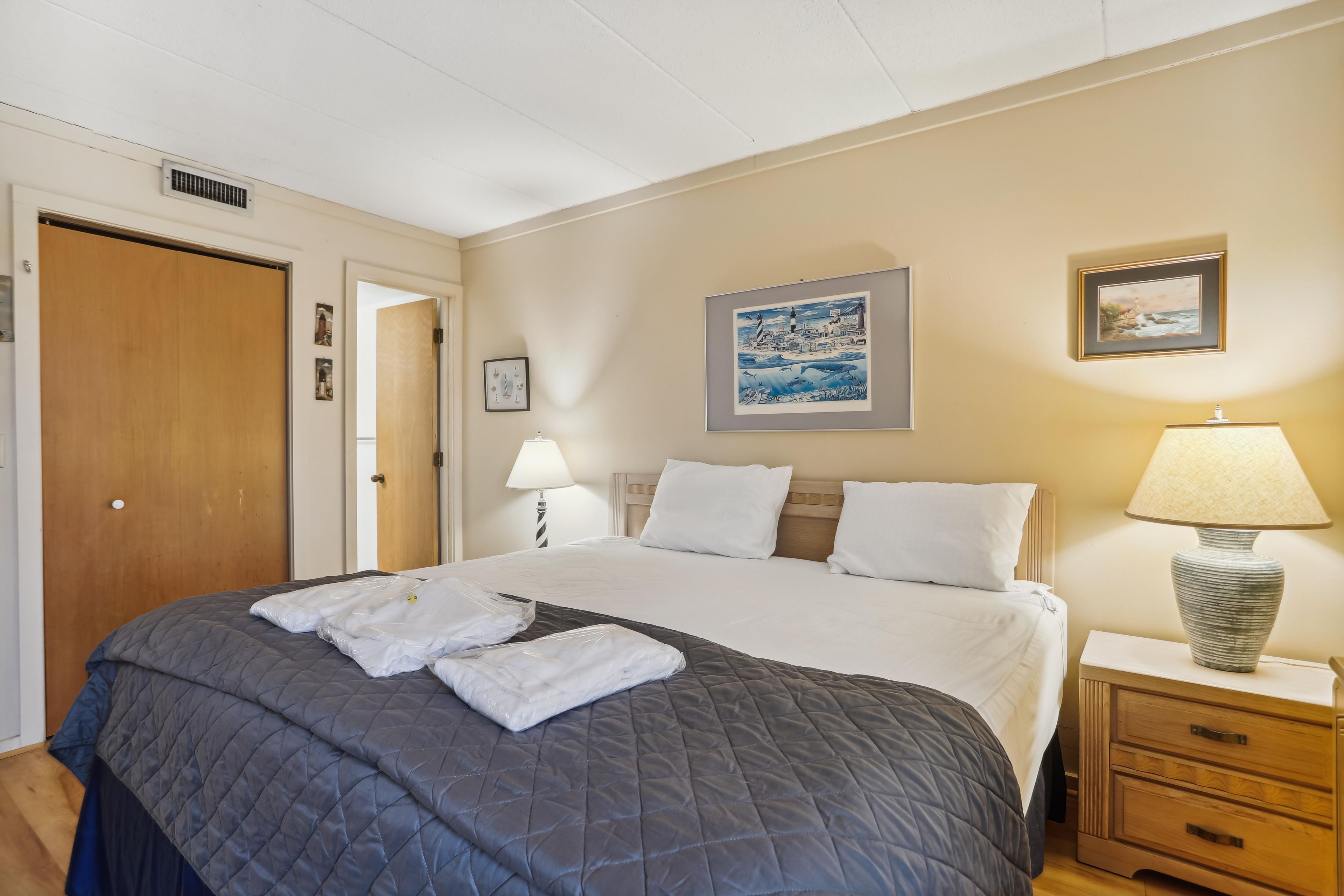Una habitación de hotel con cama, mesitas de noche, lámpara y cuadros en las paredes.