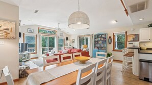 A spacious living area with a wooden dining table, white chairs, and a large window. - Leeward Inn-- Beautifully Decorated Home with Pool, Hot Tub and More! (Southern Shores)