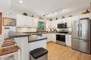 A modern kitchen with white cabinets, stainless steel appliances, a built-in oven, and a large island with a trash bin.