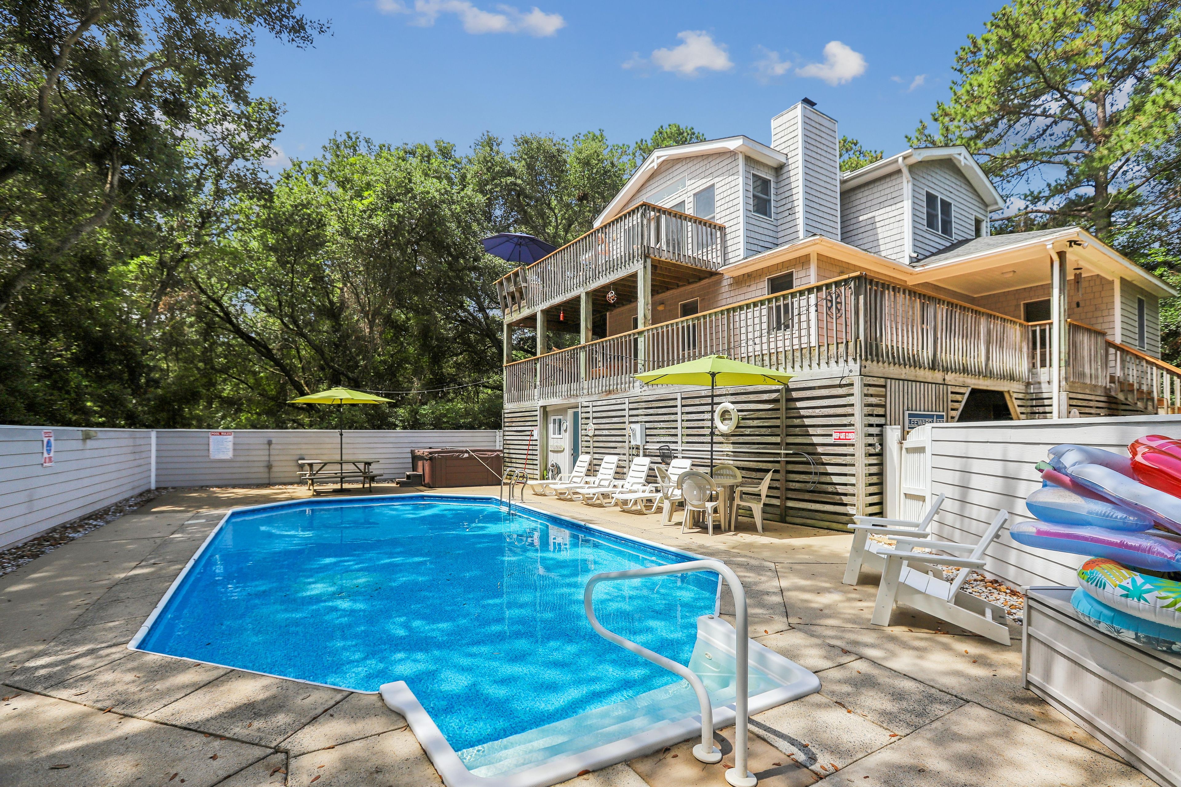 A backyard with a swimming pool, a wooden deck, and a two-story house.