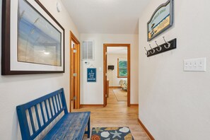 Un pasillo con un banco de madera, un cuadro enmarco, un letrero y un perchero.