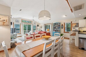 A spacious living area with a dining table, chairs, a large window, and a ceiling fan.