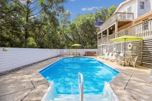 A swimming pool with a wooden deck, lounge chairs, and umbrellas.