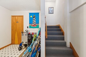 Un couloir avec une porte en bois, un porte-parapluies fixé au mur et un escalier recouvert d’une moquette à motifs.