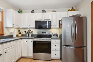 A modern kitchen with white cabinets, stainless steel appliances including a refrigerator, microwave, and oven, and a granite countertop.