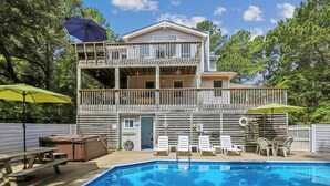 A two-story building with a pool, outdoor seating, and umbrellas. - Leeward Inn-- Beautifully Decorated Home with Pool, Hot Tub and More! (Southern Shores)