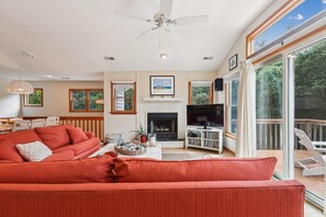 A living room with a red sofa, a fireplace, a television, and a large window with a view of trees.
