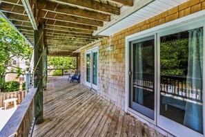 Une terrasse en bois dotée d’un espace abrité, d’une porte-fenêtre coulissante et offrant une vue sur la verdure.
