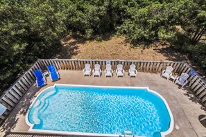 A rectangular swimming pool with a wooden deck surrounding it, equipped with lounge chairs and a ladder.