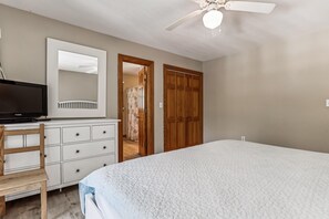 Un dormitorio con una cama, un televisor en una cómoda, una silla de madera y un armario.