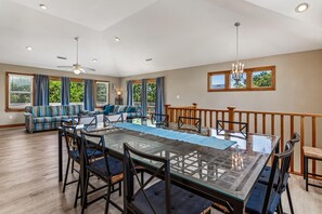 Un comedor amplio con una mesa de vidrio y sillas negras, rodeado por una sala de estar con sofá y vistas al exterior.
