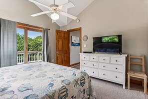 Quarto com cama, televisão, penteadeira e ventoinha no teto.