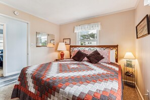 A bedroom with a large bed, a window with a view, a door, and a nightstand with a lamp.