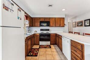 A kitchen with wooden cabinets, a stove, microwave, and a dishwasher. - Blankenship Cottage -- Pet Friendly with Sunroom and Just 2 blocks to beach (Nags Head)