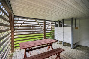 A covered outdoor area with a wooden picnic table and benches, a metal fence, and a white building with a garage door.
