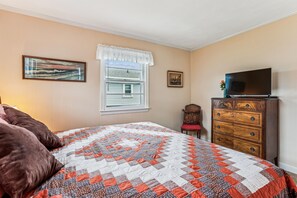 Un dormitorio con una cama, un tocador, un televisor y dos cuadros en la pared.