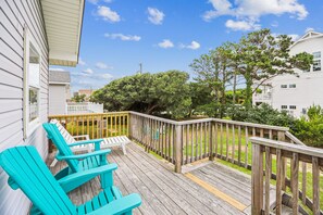 A wooden deck with two turquoise chairs, a white railing, and a view of a grassy yard and trees. - Blankenship Cottage -- Pet Friendly with Sunroom and Just 2 blocks to beach (Nags Head)