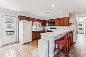 A kitchen with wooden cabinets, a refrigerator, a microwave, and a sink. - Blankenship Cottage -- Pet Friendly with Sunroom and Just 2 blocks to beach (Nags Head)