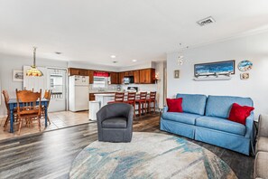 A modern living room with a blue sofa, a gray armchair, and a patterned rug. - Blankenship Cottage -- Pet Friendly with Sunroom and Just 2 blocks to beach (Nags Head)