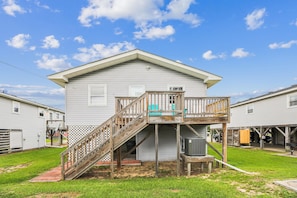 A two-story house with a wooden staircase leading to a balcony, surrounded by a grassy yard. - Blankenship Cottage -- Pet Friendly with Sunroom and Just 2 blocks to beach (Nags Head)