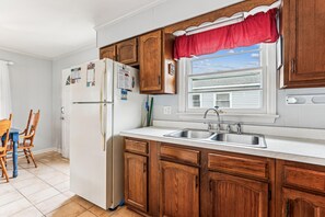 Una cocina con armarios de madera, encimera blanca, pileta doble y ventana con un toldo rojo.