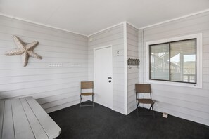 A room with white paneled walls, a starfish decoration, a bench, two chairs, a door with a number, and a window with blinds.