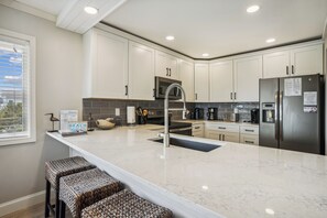 Eine moderne Küche mit weißen Schränken, einem Edelstahlkühlschrank, einer eingebauten Mikrowelle und einer großen Kücheninsel mit Barhocker.