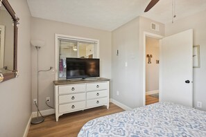 A bedroom with a bed, dresser, television, and a door leading to another room.