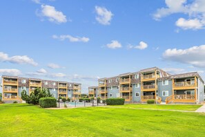 A multi-story residential building with balconies, a swimming pool, and a well-maintained lawn. - Tidewater Star -- Updated 2nd Floor Condo with Ocean Views and Pool (Duck)