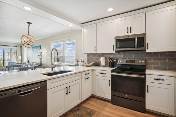 A modern kitchen with white cabinets, stainless steel appliances, and a large window.