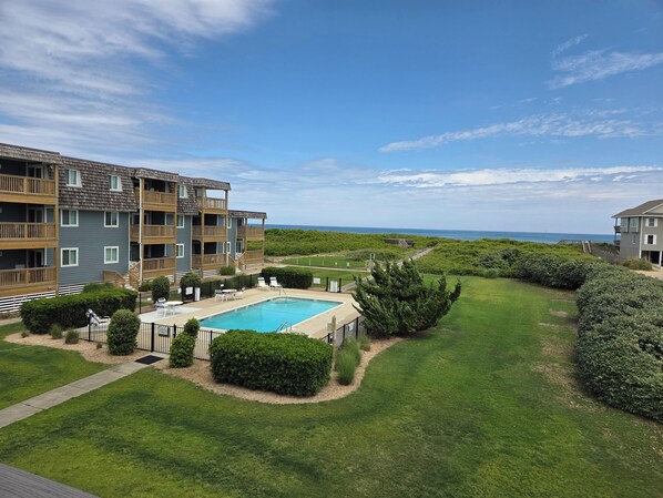 A residential building with a swimming pool, surrounded by well-maintained lawns and hedges. - Tidewater Star -- Updated 2nd Floor Condo with Ocean Views and Pool (Duck)