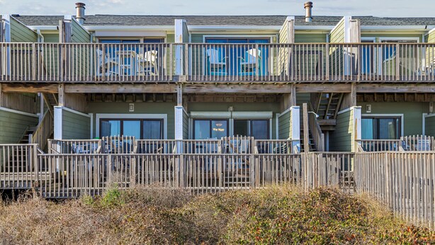 A multi-story building with balconies, a wooden fence in the foreground, and a clear sky. - Seawalk Unit 8 -- Oceanfront Townhouse with Pool Access (Kill Devil Hills)