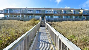 A multi-story building with a wooden walkway leading to the entrance. - Seawalk Unit 8 -- Oceanfront Townhouse with Pool Access (Kill Devil Hills)