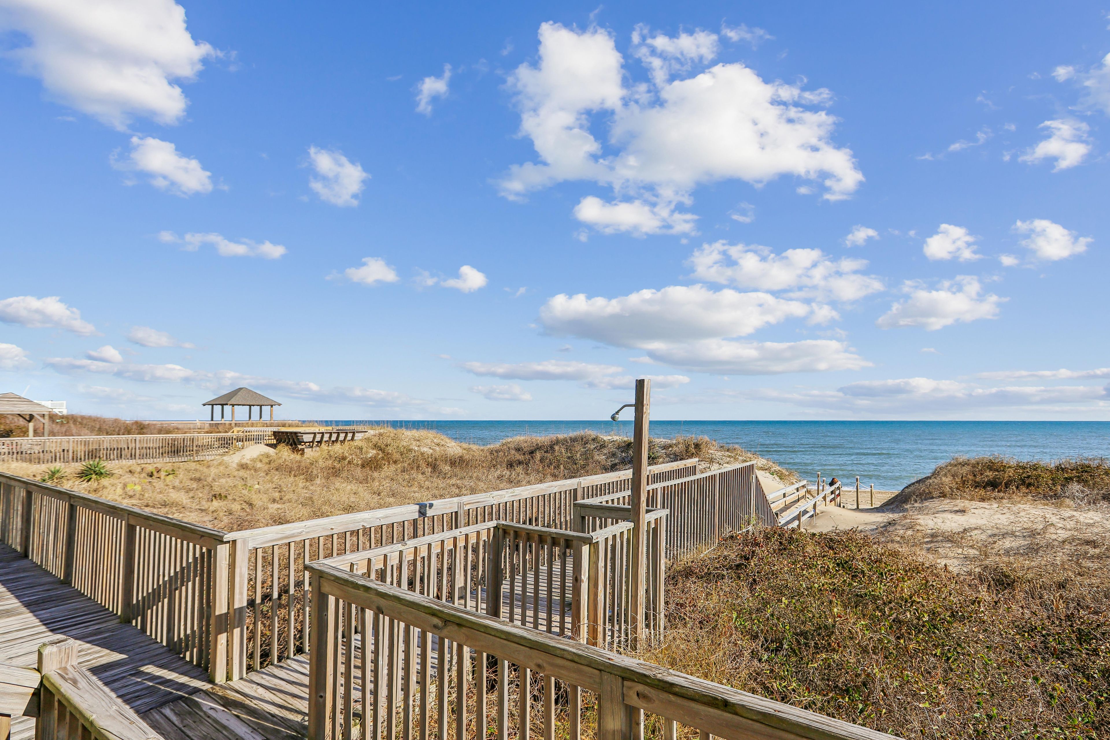 A wooden boardwalk leading to a beach with a gazebo in the background.