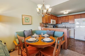 A dining area with a round table, chairs, a chandelier, wooden cabinets, a microwave, and a refrigerator. - Seawalk Unit 8 -- Oceanfront Townhouse with Pool Access (Kill Devil Hills)