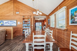 Un interior de madera con una larga mesa de comedor, sillas blancas, una estantería y un letrero de Blue Waters Seafood Co.
