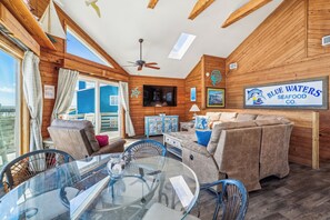 Um quarto aconchegante com paredes de madeira, uma mesa de vidro e um sofá. Há um aviso na parede para Blue Waters Seafood Co.