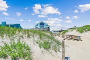 A beachfront property with a prominent blue building, sandy beach, and dune vegetation. - Freebird -- Pet Friendly Oceanfront in South Nags Head (Nags Head)