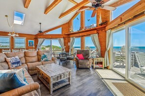 A spacious living area with a large window overlooking the ocean, furnished with a sofa, chairs, and a coffee table. - Freebird -- Pet Friendly Oceanfront in South Nags Head (Nags Head)