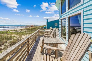 Eine Holzterrasse direkt am Strand mit Holzstühlen und -tischen, mit Blick auf das Meer und einen Steg.