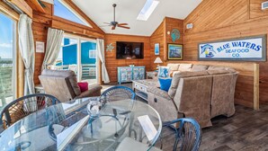 Un intérieur chaleureux avec un plafond en bois, un coin repas doté d’une table en verre et une enseigne indiquant « Blue Waters Seafood Co. ».
