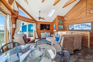 Un intérieur chaleureux avec un plafond en bois, un coin repas doté d’une table en verre et une enseigne indiquant « Blue Waters Seafood Co. ».