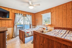 Quarto com painéis de madeira, uma cama, uma TV e um ventilador de teto.